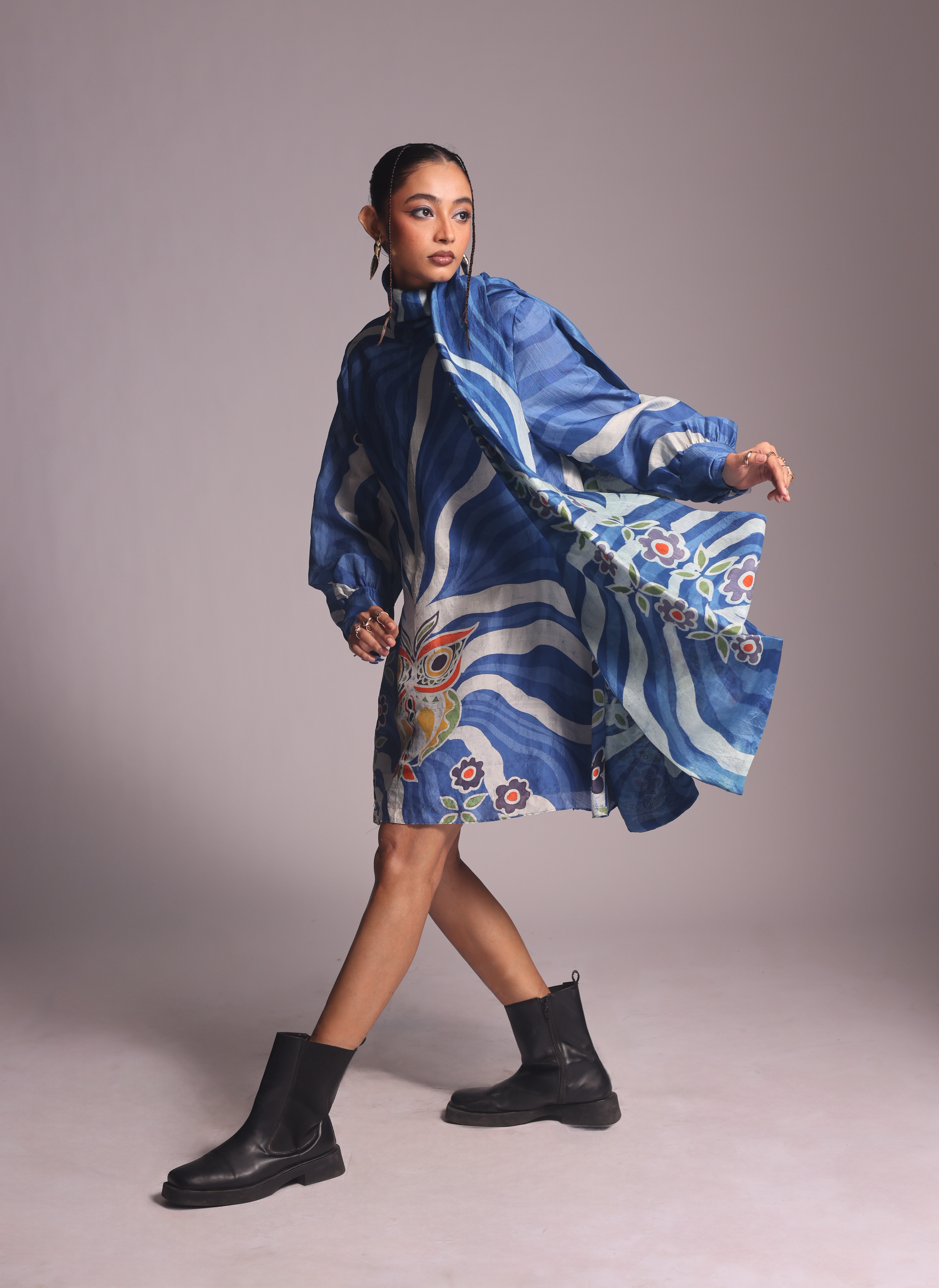 Woman wearing a blue patterned dress with black boots on a plain background